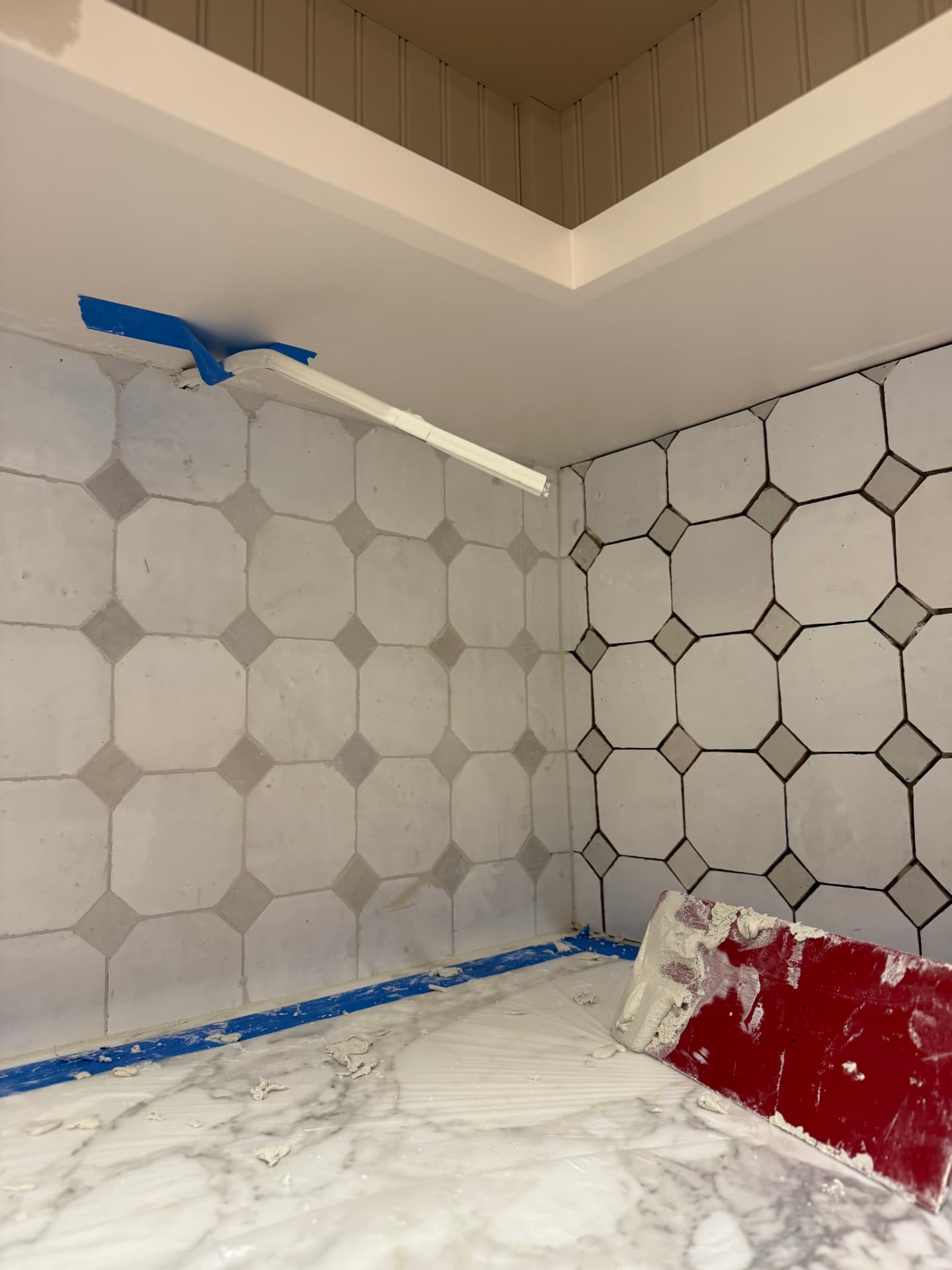 Bathroom prepped with plastic sheeting and blue painter's tape with a red grout float on the tile floor