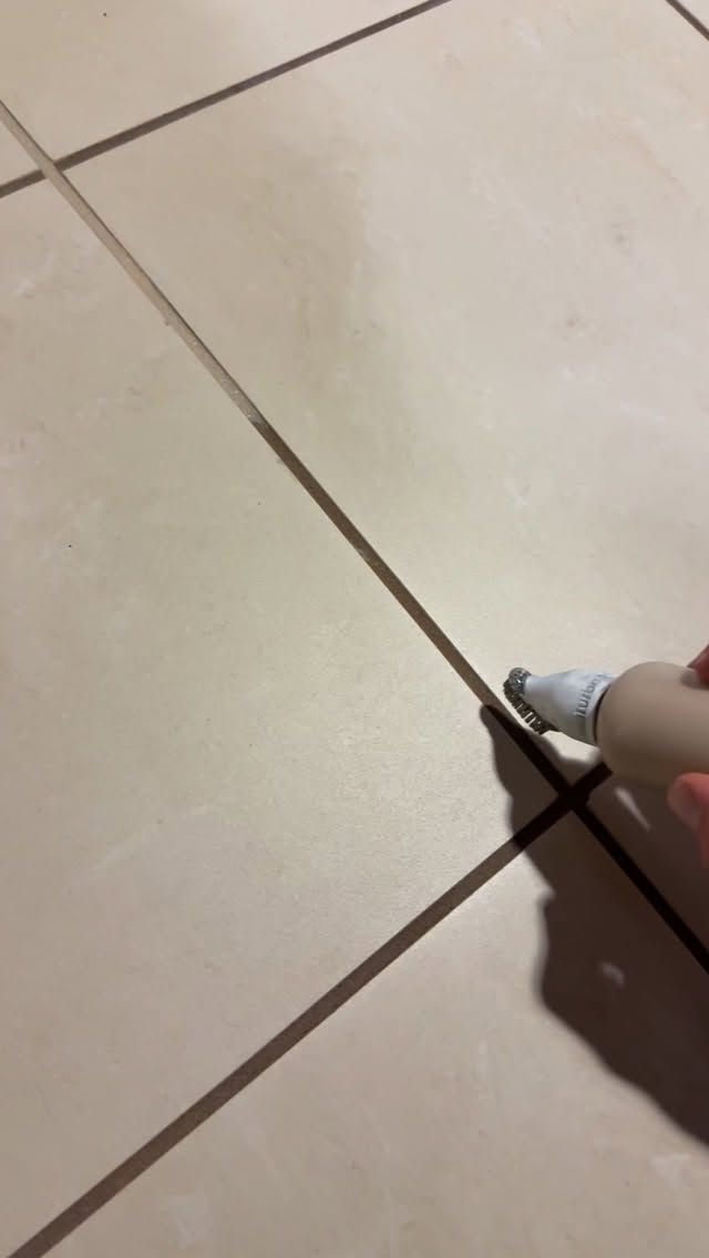 Grout pen applying fresh color to the grout lines of a beige tile floor
