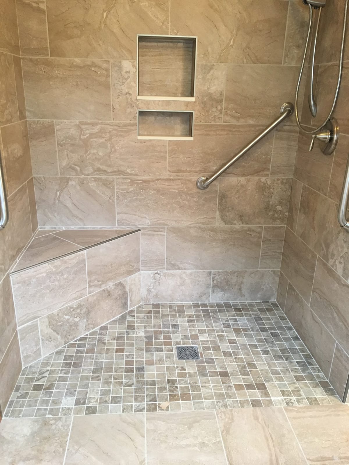 Restored tiled shower with a built-in bench, wall niches, grab bar, and mosaic tile floor